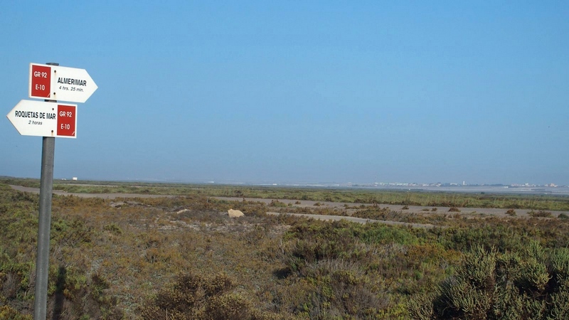 Partimos del antiguo cuartel de la Guardia Civil “Príncipe Alfonso”, hoy en ruinas y se llega al Faro del Sabinar, pasando por los charcones naturales de la primitiva albufera que dio lugar al humedal que conocemos como “Salinas de Cerrillos”. El importante ecosistema dunar será atravesado por su espacio más ancho, todo ello antes de llegar a una señal marítima que marca el extremo occidental de la Bahía de Almería. En el faro realizaremos un desvío para conocer el efecto de las extracciones de arena que se realizaron en los años 70 y 80 del siglo pasado, como el mar está ocupando estos espacios. Pasaremos por el antiguo cuartel de carabineros de Punta Sabinar, llegando hasta este vértice geográfico, donde se encuentran las antiguas instalaciones del faro. A continuación, pasando por la flecha arenosa que cerró la antigua albufera, esos arenales cada vez más raros en las costas mediterráneas, con una característica formación vegetal.  El lago artificial creado en la última fase de explotación salinera, nos permitirá acceder al cordón umbilical de las salinas con el mar: el canal de las almejas y el cabrestante que utilizando unas curiosas dragas (“las tarjillas”), lo mantenía conectado con el mar. Las instalaciones salineras, la primera elevación con un primitivo malacate (cabestrante), el resto del poblado salinero, las ruinas de los molinos o los vestigios del pantalán (pasarela flotante que se adentra en el mar y se usa como embarcadero para barcos pequeños), que existió hasta mitad del siglo pasado. El mirador de la casa de dirección es un conjunto de construcciones que hablaran a los visitantes de su pasado intenso como un lugar de gran importancia para la producción se sal. Las Salinas de Cerrillos terminan en la edificación de la segunda elevación de agua. Pasaremos junto a los nuevos estanques creados a mediados del siglo pasado y que conectarán con otras antiguas salinas, las Viejas o de la Administración, situadas junto al extremo oriental del espacio protegido, cerca de la pedanía roquetera de las Marinas. Los poco más de doce kilómetros de nuestra ruta concluirán en la tercera elevación de las salinas, al final de estas y en las inmediaciones de las Marinas y los desarrollos urbanos de Playa Serena. 